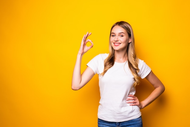 Portrait of smiling young woman okay side copy space isolated on yellow wall.