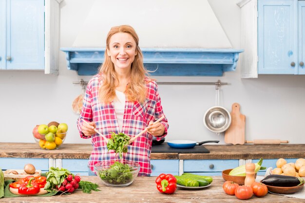 Портрет улыбающейся молодой женщины, готовящей овощной салат на кухне