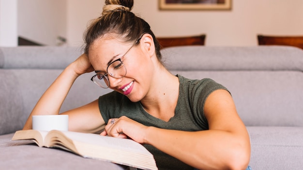 Портрет улыбающейся молодой женщины, читающей книгу дома