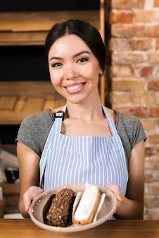 Ritratto di una giovane donna sorridente che mostra eclairs al contatore del forno
