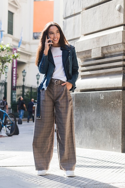 Portrait of a smiling young woman standing on street talking over mobile phone