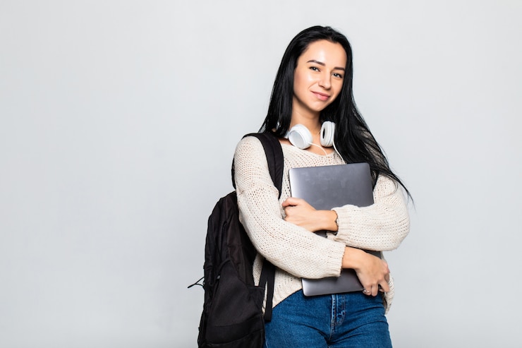 Free Photo portrait of a smiling young woman standing with laptop against gray wall
