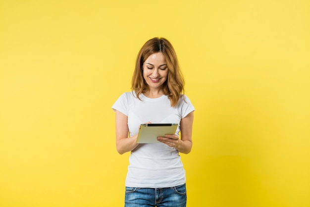 Портрет улыбающегося молодой женщины с помощью цифрового планшета на желтом фоне