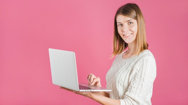 분홍색 배경에 노트북을 사용하는 웃는 젊은 여자의 초상화