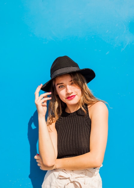 Free photo portrait of a smiling young woman wearing black hat against blue background