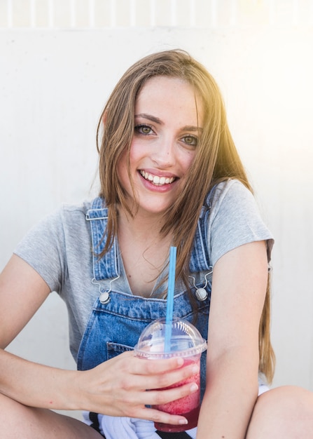 Портрет улыбающейся молодой женщины со стаканом сока, глядя на камеру