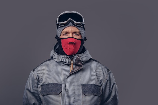 Портрет сноубордиста, одетого в полный защитный костюм для экстремального катания на сноуборде, позирующего в студии. Изолированные на сером фоне.