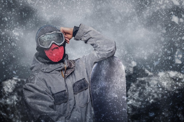 Foto gratuita ritratto di uno snowboarder vestito con un equipaggiamento protettivo completo per lo snowboard estremo in posa con lo snowboard sullo sfondo delle montagne