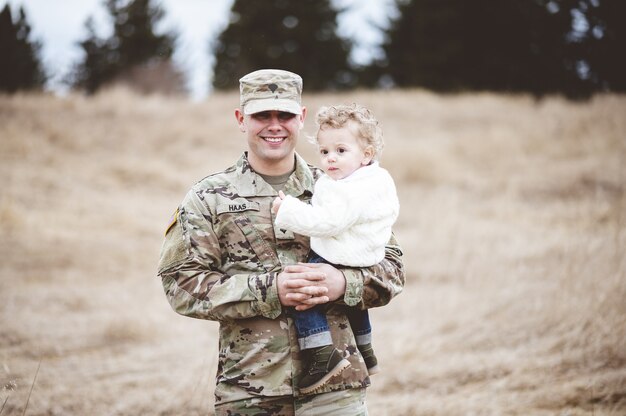 Portrait of a soldier father holding his son in a field