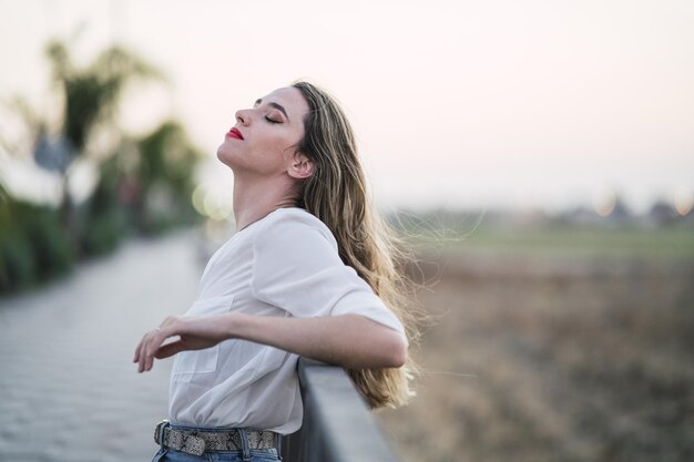 Portrait of a Spanish woman with long highlighted hair leaning on a pavement fence