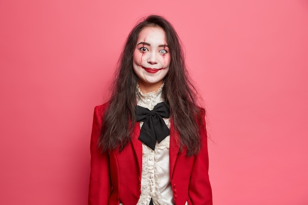 На портрете жуткой брюнетки в готическом макияже на хэллоуин изображен ужасающий вампир, идущий на вечеринку, с ужасным взглядом позирует на розовой стене