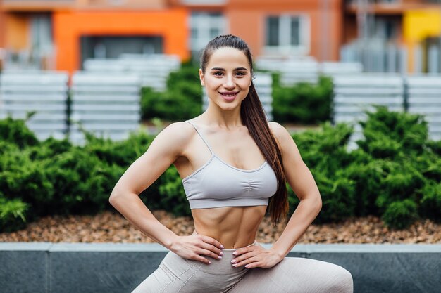 Portrait of, sportive brunette woman doing squatting exercise in street.