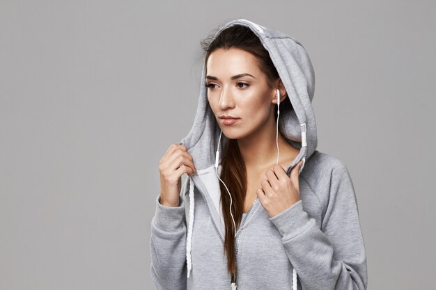 Portrait of sportive woman in hood and headphones posing on white.