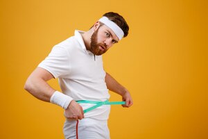 Portrait of a sports man measuring his waist with tape