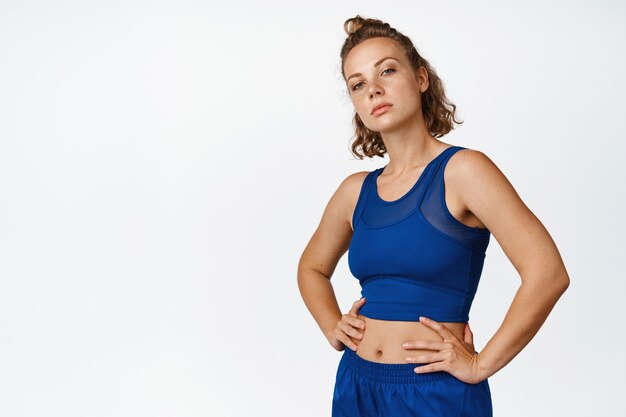 Portrait of sportswoman workout, standing confident in sportsbra with hands on waist, looking determined on white