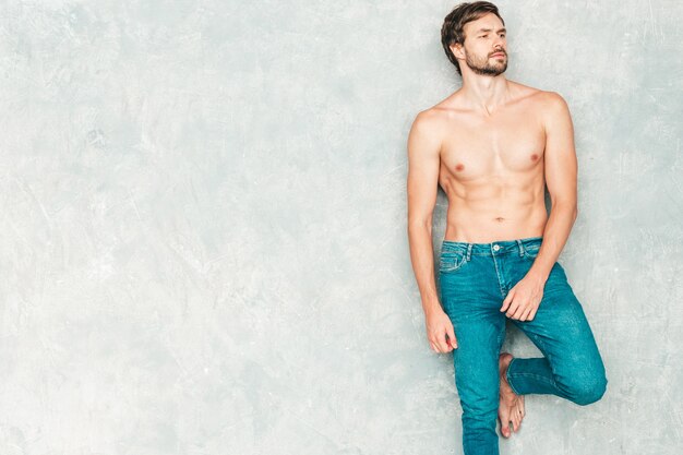 Portrait of sporty handsome strong man. Healthy smiling athletic fitness model posing near gray wall in jeans. 