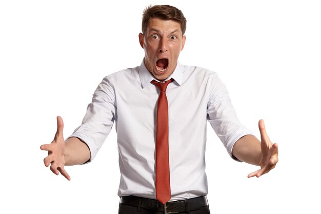 Portrait of a stately brunet guy with brown eyes, wearing in a white shirt and a red tie. He is looking very angry while posing in a studio isolated over a white background. Concept of gesticulation a