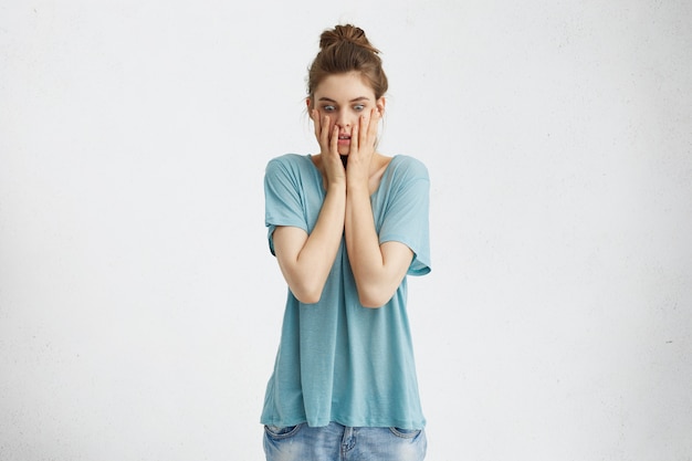 Free photo portrait of stressed woman popping eyes out and holding hands on her face, having puzzled and frustrated look as she has to speak in front of whole class, feeling afraid of public speaking