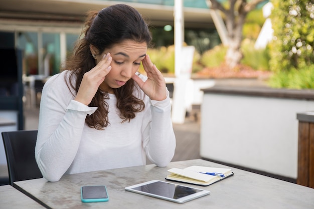 Portrait of stressed woman sitting at table with digital tablet