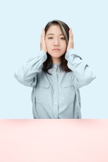 Portrait of stressed woman sitting with eyes closed and covering with hands. Isolated on blue studio background. I can not hear anything