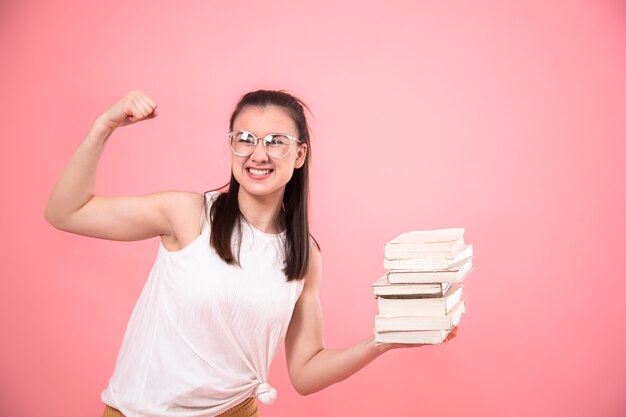 彼女の手で本を持ってポーズをとってピンクの背景に眼鏡をかけた学生の女の子の肖像画。教育と趣味の概念。