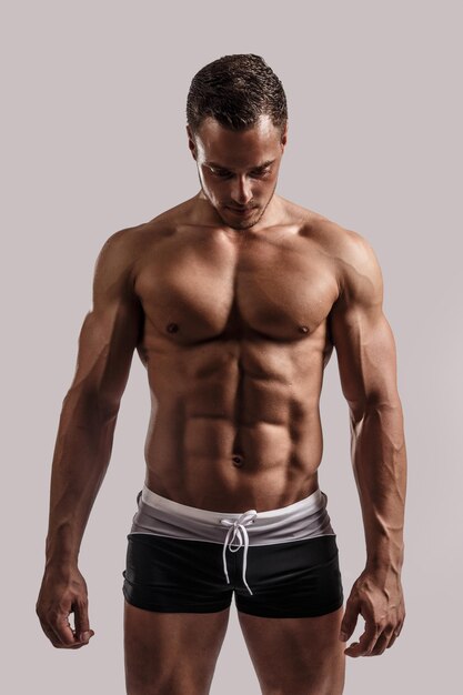 Portrait in studio of muscular male in black swimming trunks. Isolated on grey background.