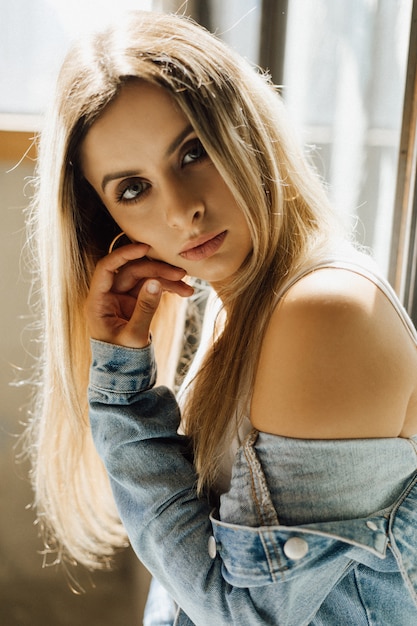 Portrait of stunning young blonde woman dressed in white top and blue casual jeans jacket