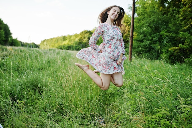 Portrait of a stunning young girl in dress jumping on the meadow