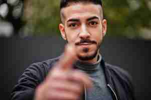 Free photo portrait of stylish arab beard man wear grey turtleneck and black jaket arabian model guy show finger close to camera