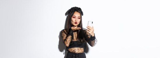Ritratto di elegante blogger femminile asiatico con trucco gotico e costume di halloween che invia un bacio d'aria a