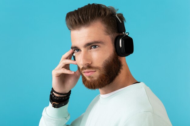 Portrait of stylish attractive young bearded man listening to music on wireless headphones modern style confident mood 