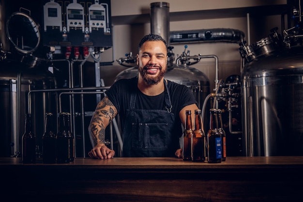 Free photo portrait of a stylish bearded dark skinned male with a tattoo on his hand standing behind the counter in a brewery.