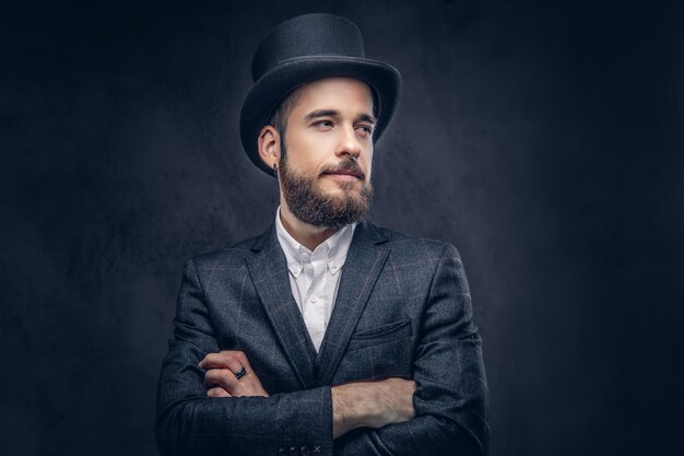 Portrait of a stylish bearded male in an elegant suit and cylinder hat, over dark background.