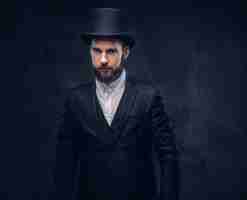 Free photo portrait of a stylish bearded male in an elegant suit and cylinder hat, looking at a camera over dark background.