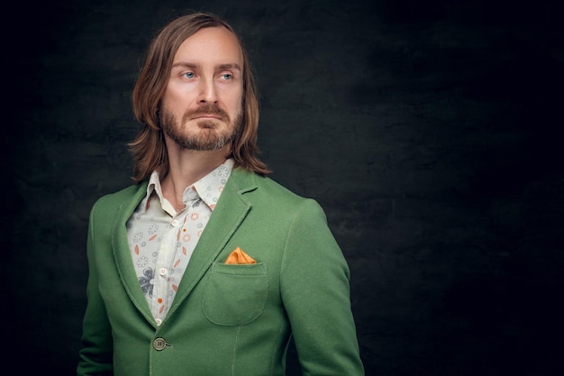Portrait of a stylish bearded male with long hair dressed in a green jacket.