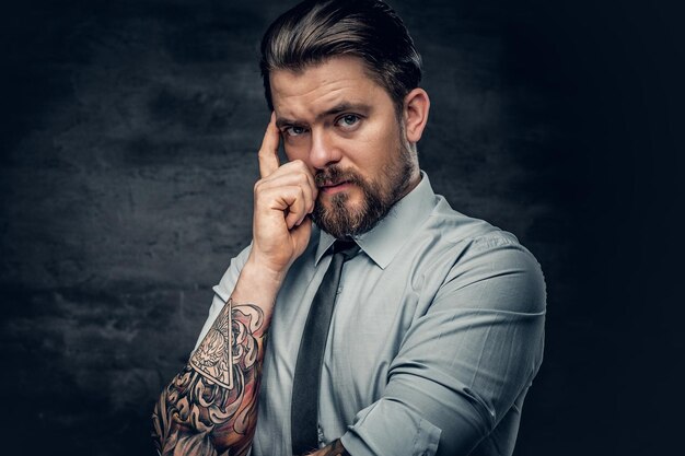 Portrait of a stylish bearded male with tattoos on his arm, dressed in a white shirt and a tie.