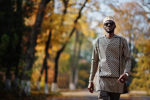 Portrait of stylish black african american man at hat and sunglasses against sunny autumn fall background Rich people in africa at traditional dress