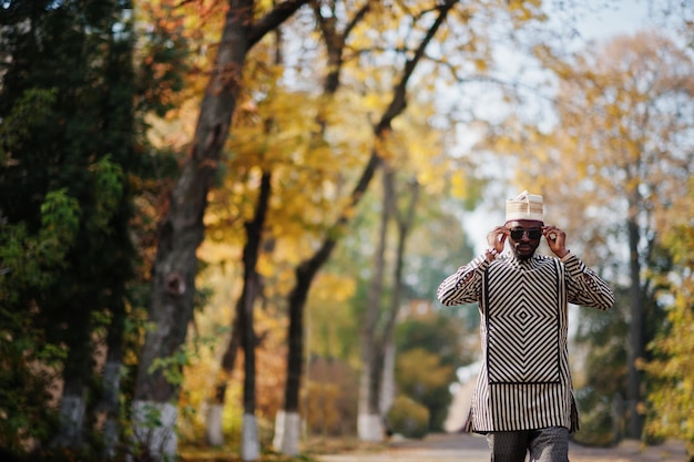 Portrait of stylish black african american man at hat and sunglasses against sunny autumn fall background Rich people in africa at traditional dress