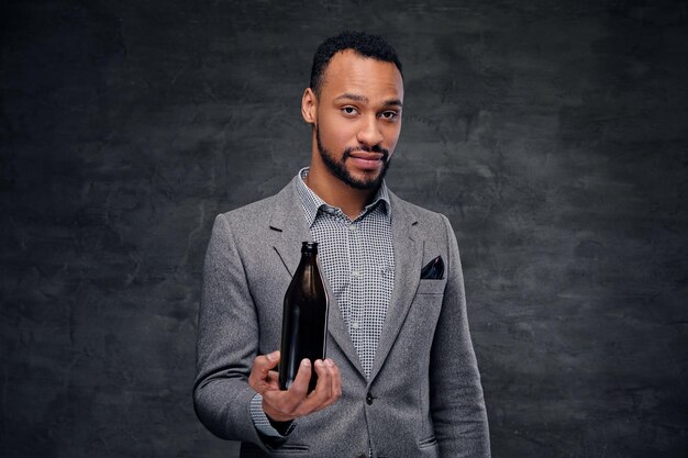 Portrait of stylish black American male dressed in a grey suit holds a craft beer bottle.