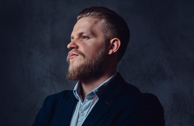 Portrait of stylish blond bearded male dressed in a suit over grey background.