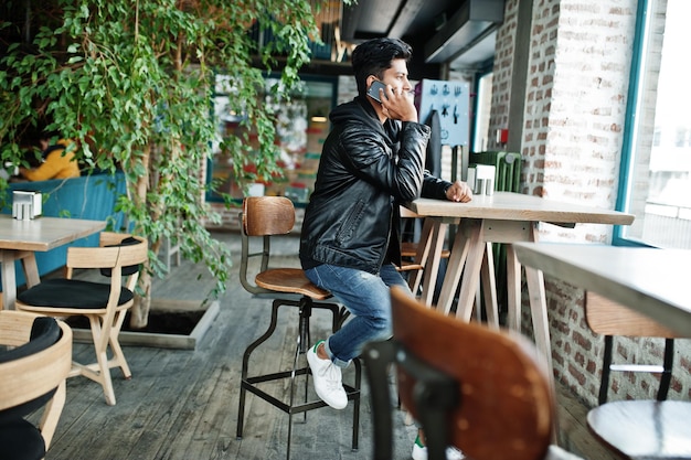 Portrait of stylish and casual young asian man wear on leather jacket spending time at cafe and speaking on mobile phone