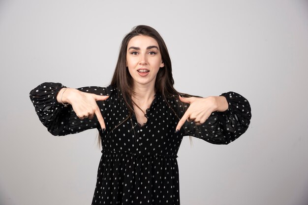 Portrait of stylish charming girl with long hair pointing down.