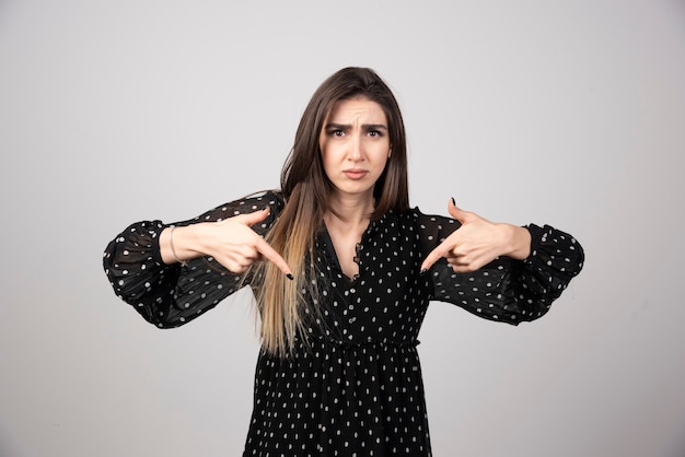 Portrait of stylish charming girl with long hair pointing down.