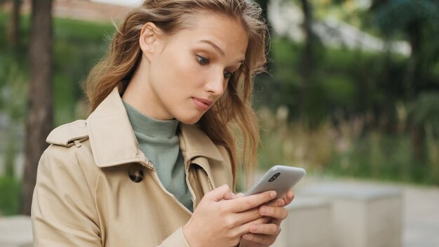 公園で休んでいるスマートフォン屋外女子学生のメッセージに驚いて答えて見えるスタイリッシュな女の子の肖像画