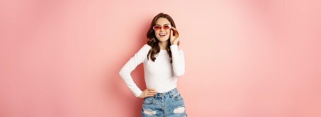 Foto gratuita ritratto di ragazza glamour alla moda in occhiali da sole che ride e sorride in piedi sopra il backgrou rosa delle vacanze