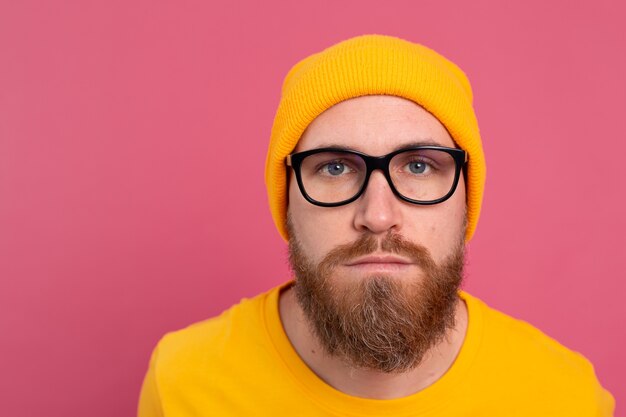 Portrait of stylish handsome european bearded man in casual yellow shirt hat and glasses on pink