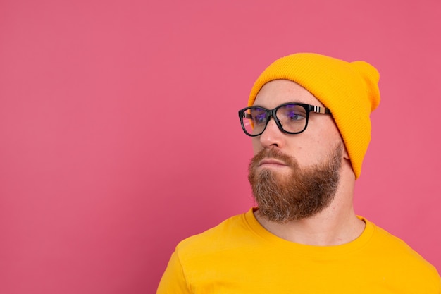 Portrait of stylish handsome european bearded man in casual yellow shirt hat and glasses on pink