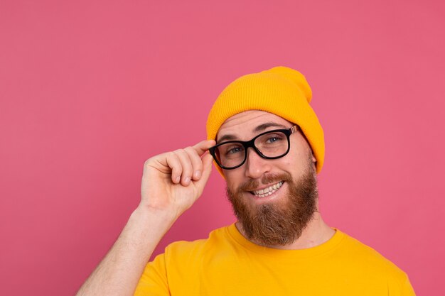 Portrait of stylish handsome european bearded man in casual yellow shirt hat and glasses on pink