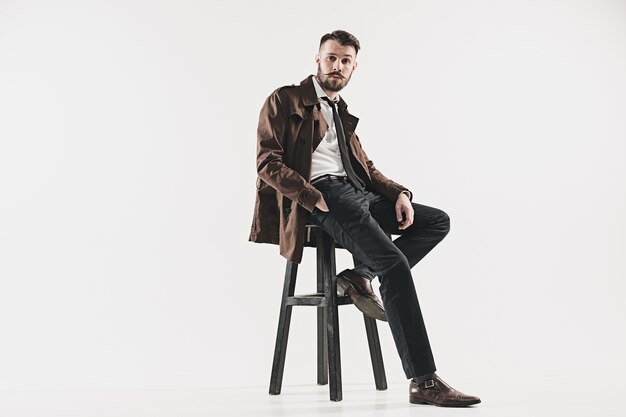 Portrait of stylish handsome young man sitting against white. Man wearing jacket