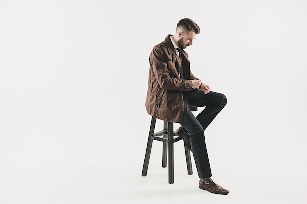 Portrait of stylish handsome young man sitting at studio against white. Man wearing jacket